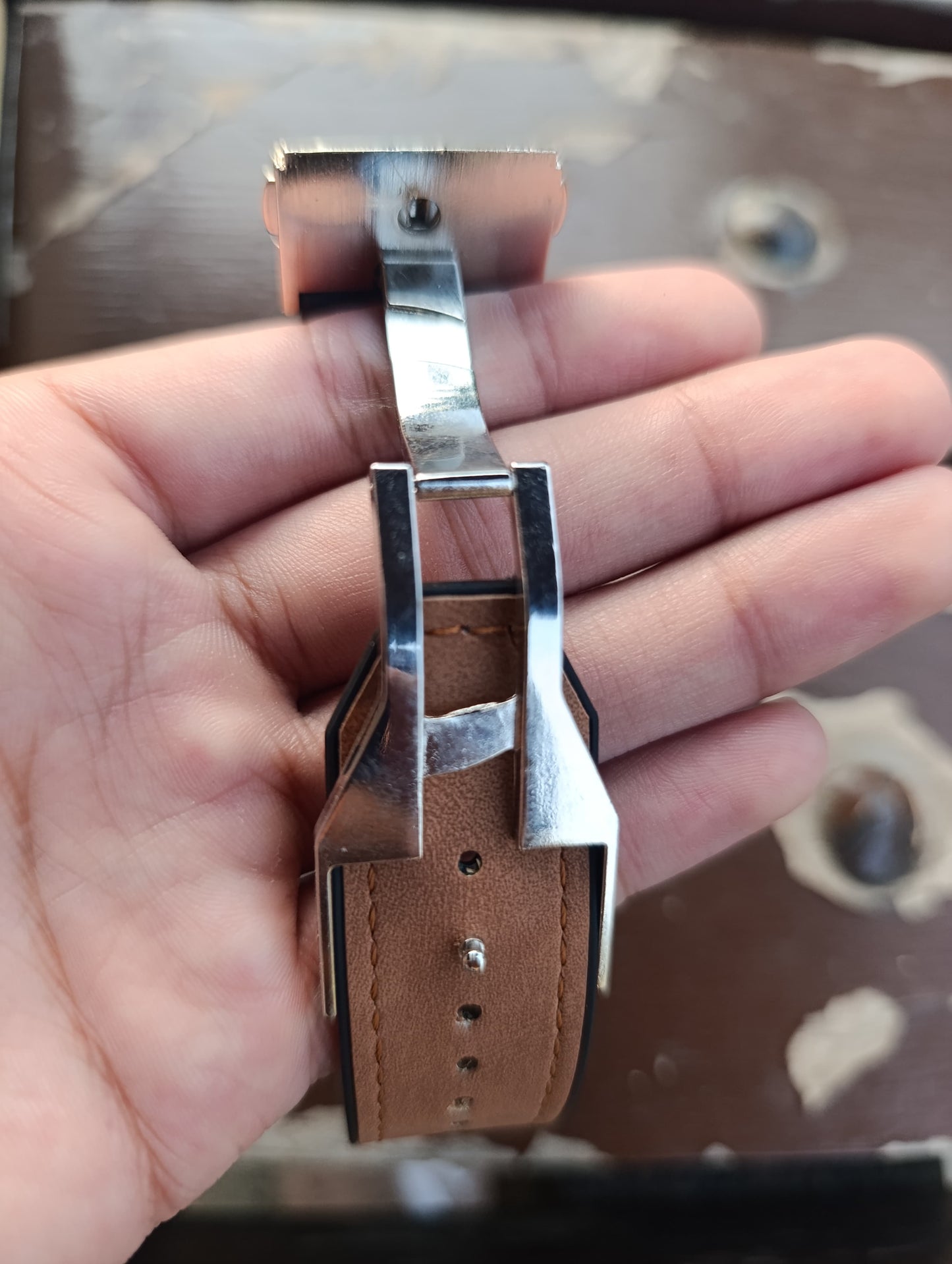 Close-up of a hand holding a watch strap with a brown leather band and silver clasp.