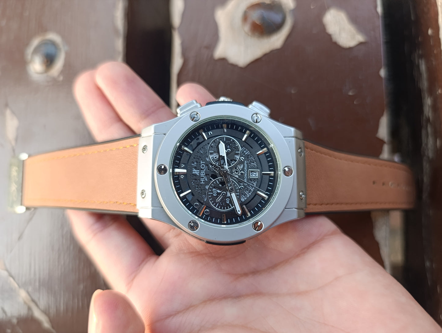 Hand holding a watch with a brown leather strap against a textured surface