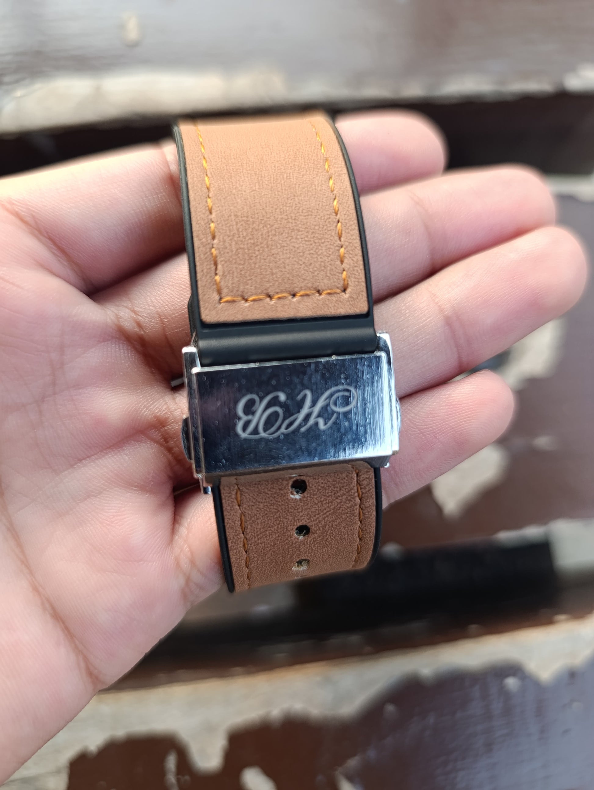 Brown leather belt with silver buckle held by a hand against a blurred background