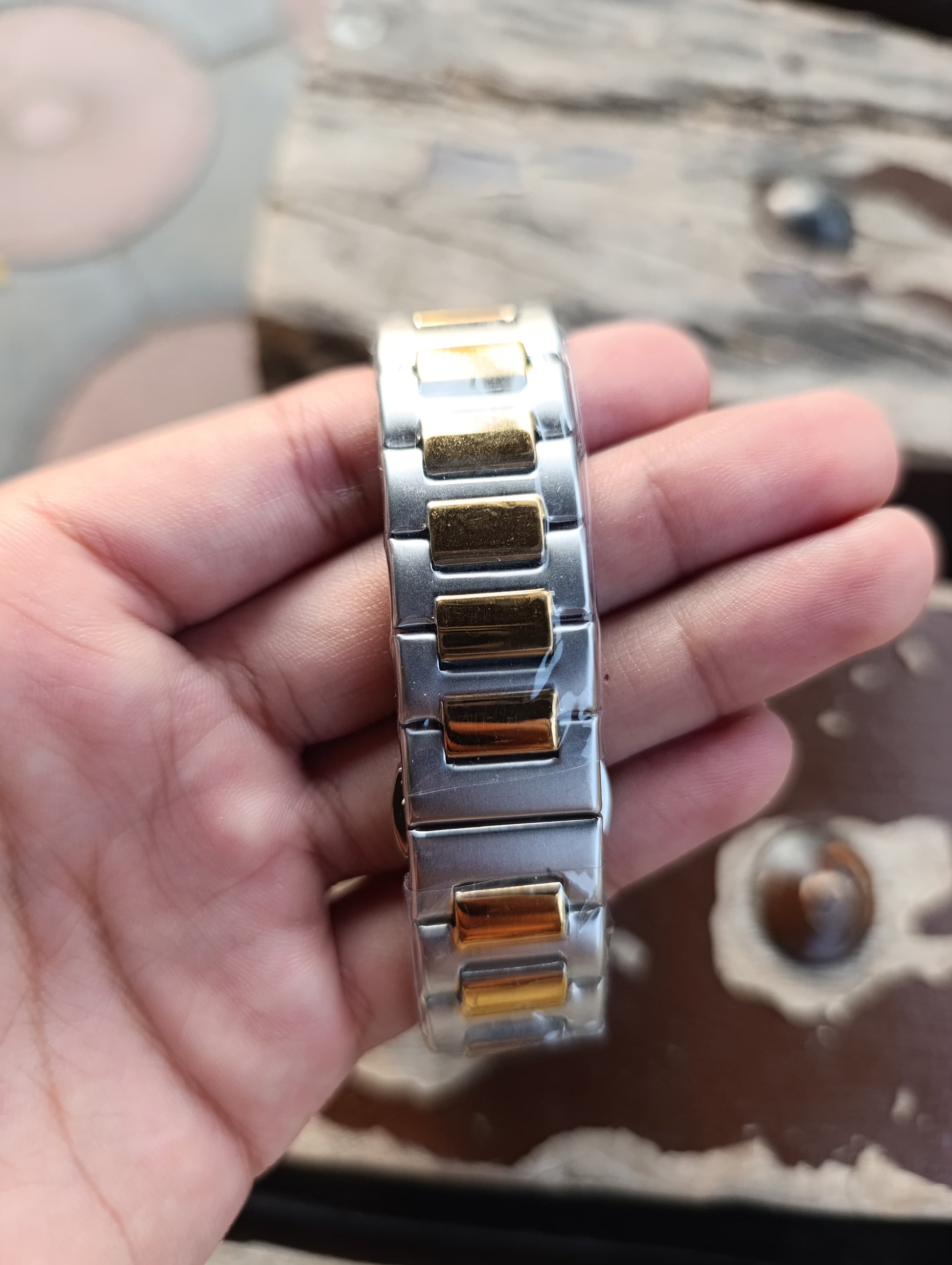 Silver and gold watch band held in a hand with a blurred background