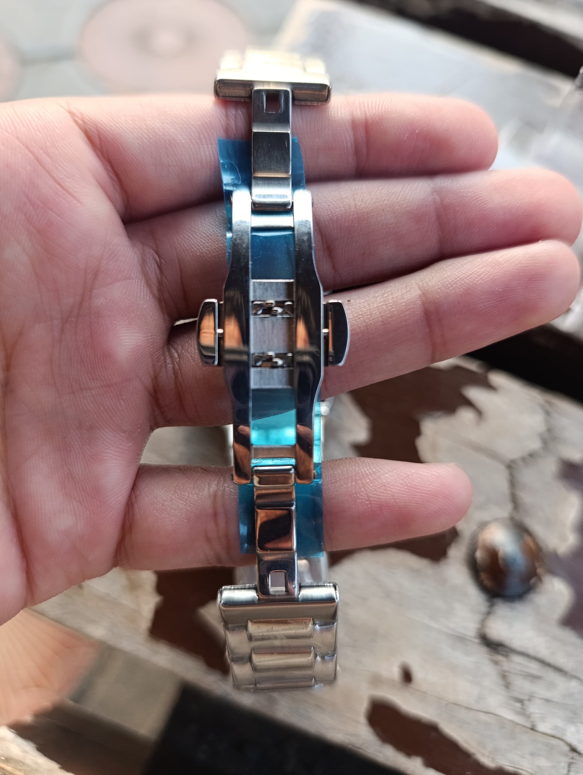 Metallic watch strap held in a hand with a blurred background