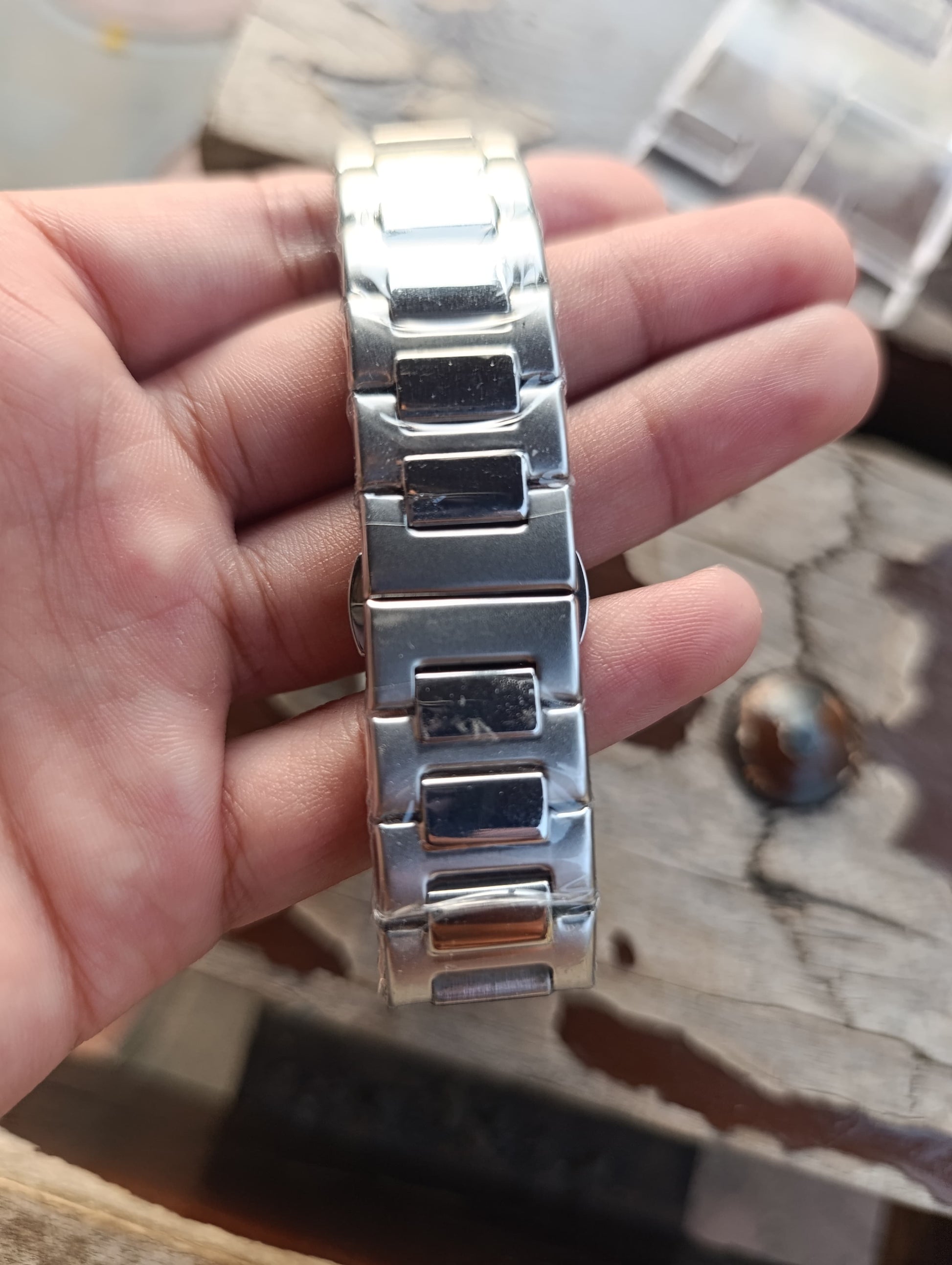 Silver watch strap held in a hand on a wooden surface