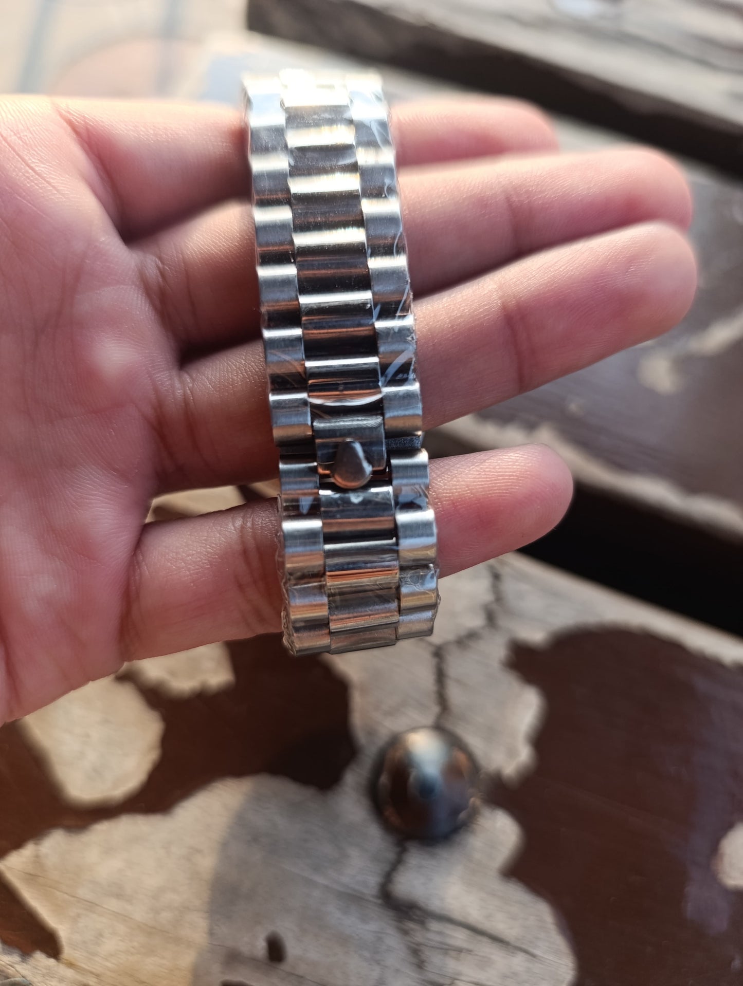 Silver watch band held in a hand on a wooden surface