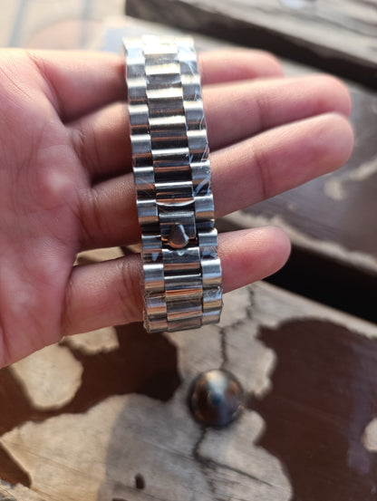 Silver watch band held in a hand on a wooden surface
