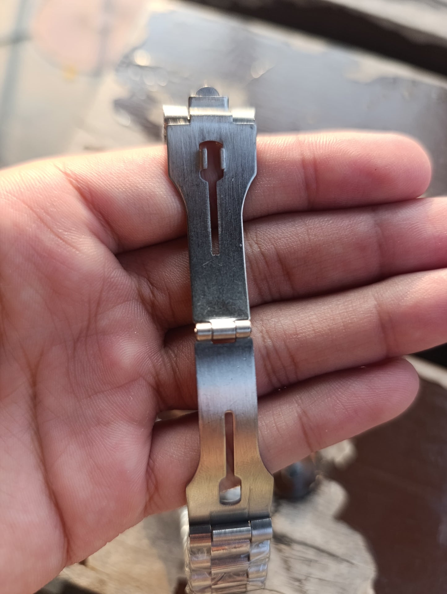 Metallic watch strap extension held between fingers with a blurred background