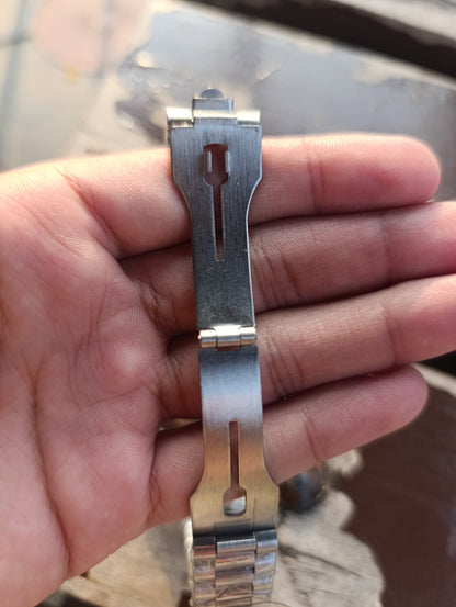 Metallic watch strap extension held between fingers with a blurred background